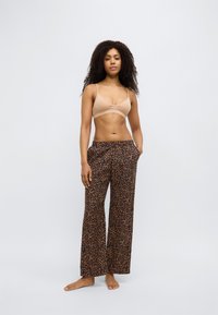 Bralette beige à fines bretelles associée à un pantalon à jambes larges avec un imprimé léopard marron. Le tissu semble léger et doux.