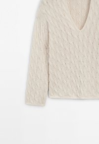 Pull en maille torsadée de couleur crème avec manches longues et col en V, présenté sur un fond blanc.