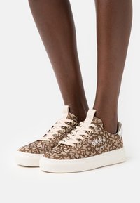 Bruna mönstrade kanvas sneakers med beiga snören och vita logodetaljer. Gummisula och silverdetaljer på hälen.