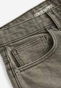 Graue Jeans aus Denim mit sichtbarem Vorderfach, gesteppten Details und einem Markenlabel amBund. Hat eine glatte Textur.