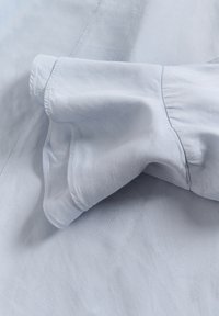 Detailní záběr na světle modrou tkaninu s viditelnými švy a záhyby, ukazující texturu a detaily šití.