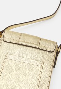 Borsa a tracolla in pelle granulosa dorata, piccola, con tasca frontale a soffietto e tracolla regolabile, su sfondo bianco.