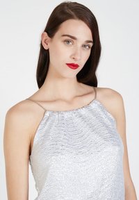 Top plateado con cuello halter de tela texturizada, que presenta un escote fruncido y tirantes metálicos finos. Superficie suave y brillante.