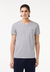 Szary t-shirt z krótkim rękawem w kształcie litery V, wykonany z miękkiego materiału, z małym zielonym logo krokodyla na lewej piersi. Prosty i klasyczny design.