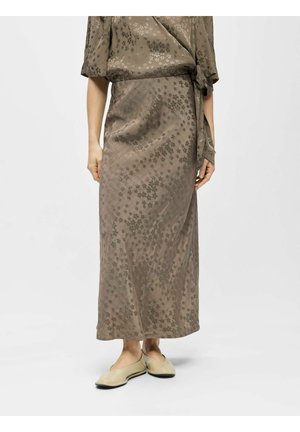 Femme portant une jupe portefeuille fleurie taupe avec un haut assorti et des chaussures plates beiges, debout devant un fond clair uni.