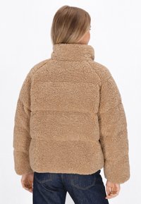 Beige fleecejakke med h�øj krave. Har en tekstureret, fluffy overflade og en afslappet pasform. Synlige søm linjer løber vandret over jakken.