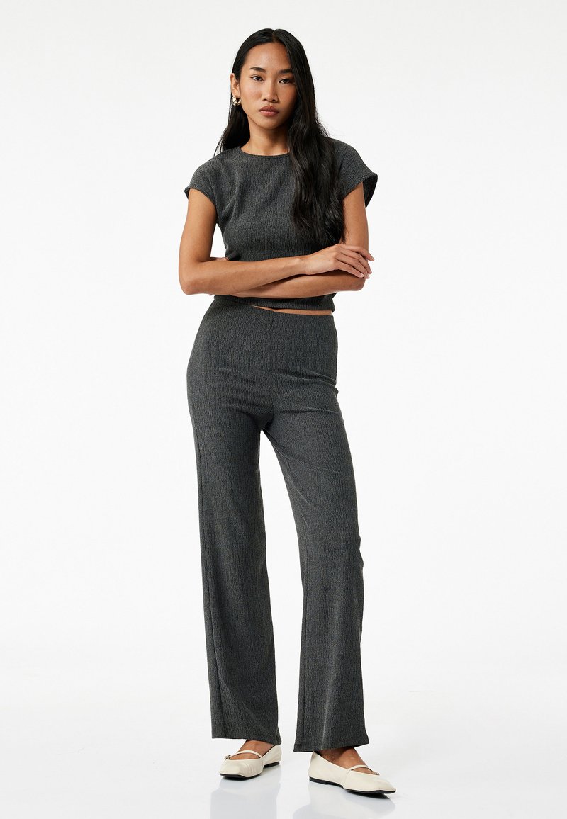 Grijze gebreide twee-delige set met een kort mouw crop top en high-waisted, wijde broek. Zachte textuur met subtiele verticale lijnen.
