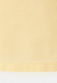 Tissu beige avec une texture de tissage visible et un ourlet cousu horizontalement près du bord inférieur.