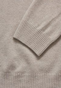 Pull en maille beige avec des poignets et un ourlet côtelés. Texture douce, avec une surface lisse et une couleur claire, idéale pour une superposition décontractée.