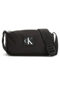 Czarna nylonowa torba na ramię w prostokątnym kształcie, z zamkiem błyskawicznym, regulowanym paskiem i kontrastującą białą naszywką z logo.