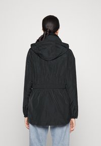 Černá lehká bunda s kapucí, elastickým pasem a nařasenými manžetami. Hladká textilie a minimalistický design. Žádné viditelné vzory ani akcenty.