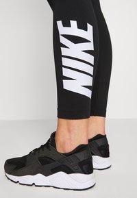 Black leggings with a large white "NIKE" logo on the side, paired with black and white athletic shoes featuring a textured heel and lace closure.