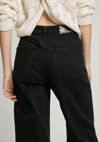 Svarta denimjeans med en figurnära design, som har två bakfickor, subtila sömdetaljer och en märkesetikett på midjebandet.