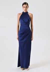 Navy Satin-Maxi-Kleid mit Neckholder, tailliertem Schnitt, seitlicher Drapierung und einer glatten, fließenden Textur. Kombiniert mit hellen Schuhen.
