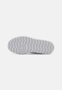 Semelle de chaussure en caoutchouc blanche avec un motif ondulé, présentant un logo circulaire au centre et du texte autour du périmètre.