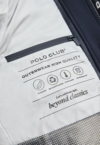 Wnętrze lekkiej kurtki w kolorze szarym z kieszenią, metkami dotyczącymi pielęgnacji tkanin oraz znakowaniem; wykonana z materiału z recyklingu, zapewniająca ciepło oraz odporność na wodę.