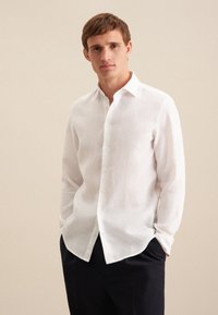 Camicia bianca in lino con colletto classico, maniche lunghe e vestibilità rilassata; presenta una texture sottile e cinque bottoni sul davanti.