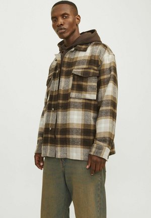 Brown and cream plaid flannel shirt with chest pockets, button closure, and relaxed fit, layered over a dark hooded sweatshirt.