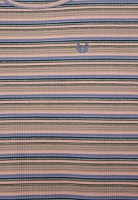 Koszulka w paski, prążkowana, w pastelowych kolorach różowym, lawendowym, zielonym i granatowym. Posiada mały niebieski emblemat na piersi, okrągły dekolt oraz teksturowany materiał.