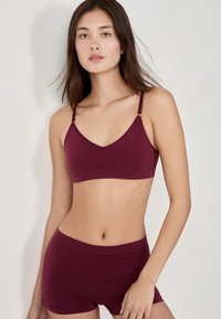 Burgundowy biustonosz braletka z regulowanymi ramiączkami i gładkim, bezszwowym wzornictwem. Zestawiony z dopasowanymi szortami w tym samym kolorze, wykonanymi z miękkiego materiału.