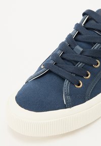 Marinblå canvas sneakers med vit gummisula, rund tå, gyllene ögla och texturerade snörningar. Har en slät läderdetalj på sidan.
