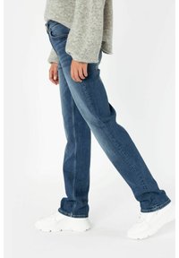 Tmavě modré džínové kalhoty s rovný střih, minimálním odřením a kontrastním šitím, doplněné bílými robustními teniskami.