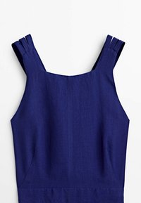 Ärmlös mörkblå linnekjol med breda remmar som har tre veck vid axlarna och en fyrkantig halsringning.