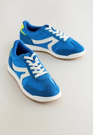 Modré tenisky z semišu a textilu, s bielymi akcentmi, štruktúrovaným povrchom a podrážkou z gumy. Šnúrky sú biele; na zadnej strane je neonovo zelený detail.