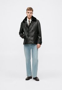 Veste noire en cuir à double boutonnage avec une finition texturée et un col en fausse fourrure, assortie à un jean droit bleu clair et des chaussures noires.