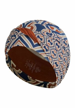 Coiffure style turban avec motifs géométriques bleus, blancs et rouille et un détail torsadé en tissu uni rouille sur un côté.