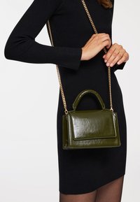 Borsa a tracolla in pelle verniciata verde con manico superiore e tracolla in catena dorata regolabile. Presenta una pattina frontale e una superficie testurizzata.