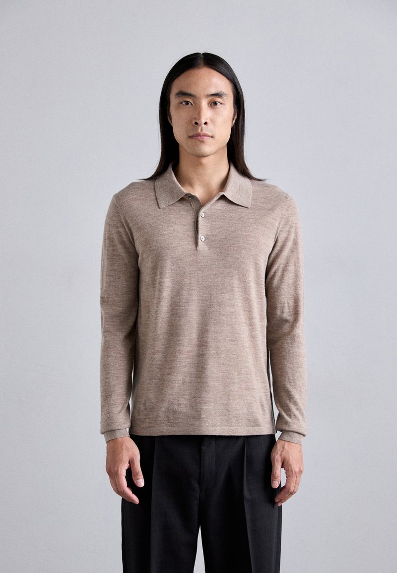 Polo shirt beige a maniche lunghe realizzato in tessuto testurizzato, con colletto, patta con tre bottoni e una vestibilità rilassata, abbinato a pantaloni scuri.