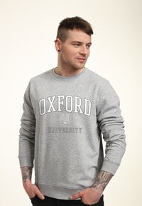 Felpa grigia con la scritta "OXFORD UNIVERSITY" stampata in nero. Presenta un classico collo a giro e maniche lunghe. Tessuto morbido.