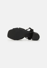 Mustat mokka-korkokengät, joissa on leveä nauha jalan yli, säädettävä nilkkahihna ja hieman terävä nenä. Teksturoitu pohja.