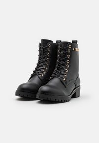 Stivali alla caviglia in pelle nera con occhiali in metallo dorato e borchie decorative. Presentano una suola spessa e testurizzata e un design con lacci sul davanti.