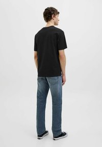 Schwarzes Baumwoll-T-Shirt mit kurzen Ärmeln, Rundhalsausschnitt, lockerer Passform, kombiniert mit hellblauen Jeans und schwarzen Leinenschuhen.
