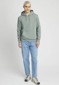 Sweat-shirt à capuche vert clair avec poche kangourou, associé à un jean droit bleu clair et des baskets grises.