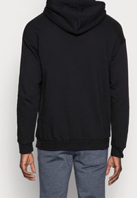 Felpa nera con cappuccio, maniche lunghe, polsini e orlo a coste. Realizzata in morbido materiale, presenta una cucitura sul retro e una vestibilità comoda.