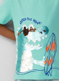 Turkusowa bawełniana koszulka z cekinowym wzorem przedstawiającym falę oraz deskę surfingową z pomarańczowymi akcentami. Tekst brzmi "CHWYTASZ FALĘ!" w niebieskim kolorze.