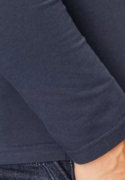 Maglietta a maniche lunghe blu navy con un design aderente, texture liscia e orlo cucito. Dettaglio ravvicinato della manica.