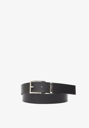 Cintura nera in pelle con fibbia rettangolare argentata e anello metallico inciso con la scritta "GUESS", arrotolata su uno sfondo bianco.