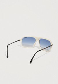 Gafas de sol con marco blanco, lentes degradados azules y brazos curvados negros, descansando sobre una superficie clara.