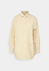 Chemise beige à manches longues avec boutons, col classique et poignets, présentée sur un fond gris clair uni.