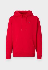 Sudadera con capucha roja hecha de algodón, con un bolsillo tipo canguro en la parte frontal, cordones y una pequeña parche con logo en el pecho izquierdo.