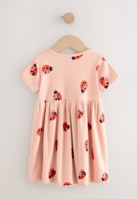 Robe rose à manches courtes pour tout-petit avec des imprimés de coccinelles rouges et noires, suspendue sur un cintre en bois sur fond blanc.
