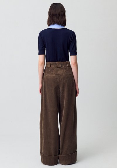 Top blu navy a maniche corte con colletto azzurro; pantaloni in corda a gamba larga marroni con vita alta e orli arrotolati.
