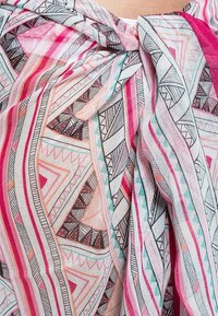 Gros plan sur un tissu avec des motifs géométriques colorés en rose, rouge, sarcelle et noir, torsadé en un nœud près du centre supérieur.