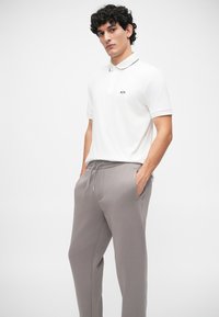 Cămașă polo albă cu guler negru și logo, asociată cu pantaloni de trening gri, cu talie elastică și buzunare laterale.