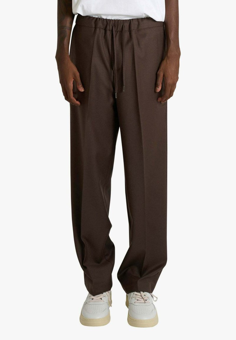 Pantaloni marroni a gamba larga con vita elastica e coulisse, dalla texture liscia, abbinati a sneakers bianche.