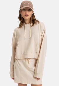 Cream cropped hoodie with a front pocket, drawstring, and embroidered detail. Paired with a matching beige miniskirt with a side pocket.